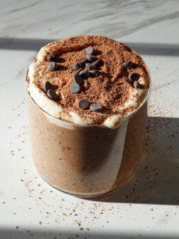 Tiramisu overnight oats in a glass jar topped with yogurt, cocoa powder, and mini chocolate chips