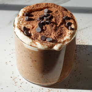 Tiramisu overnight oats in a glass jar topped with yogurt, cocoa powder, and mini chocolate chips