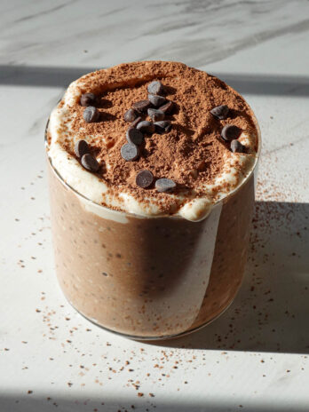Tiramisu overnight oats in a glass jar topped with yogurt, cocoa powder, and mini chocolate chips