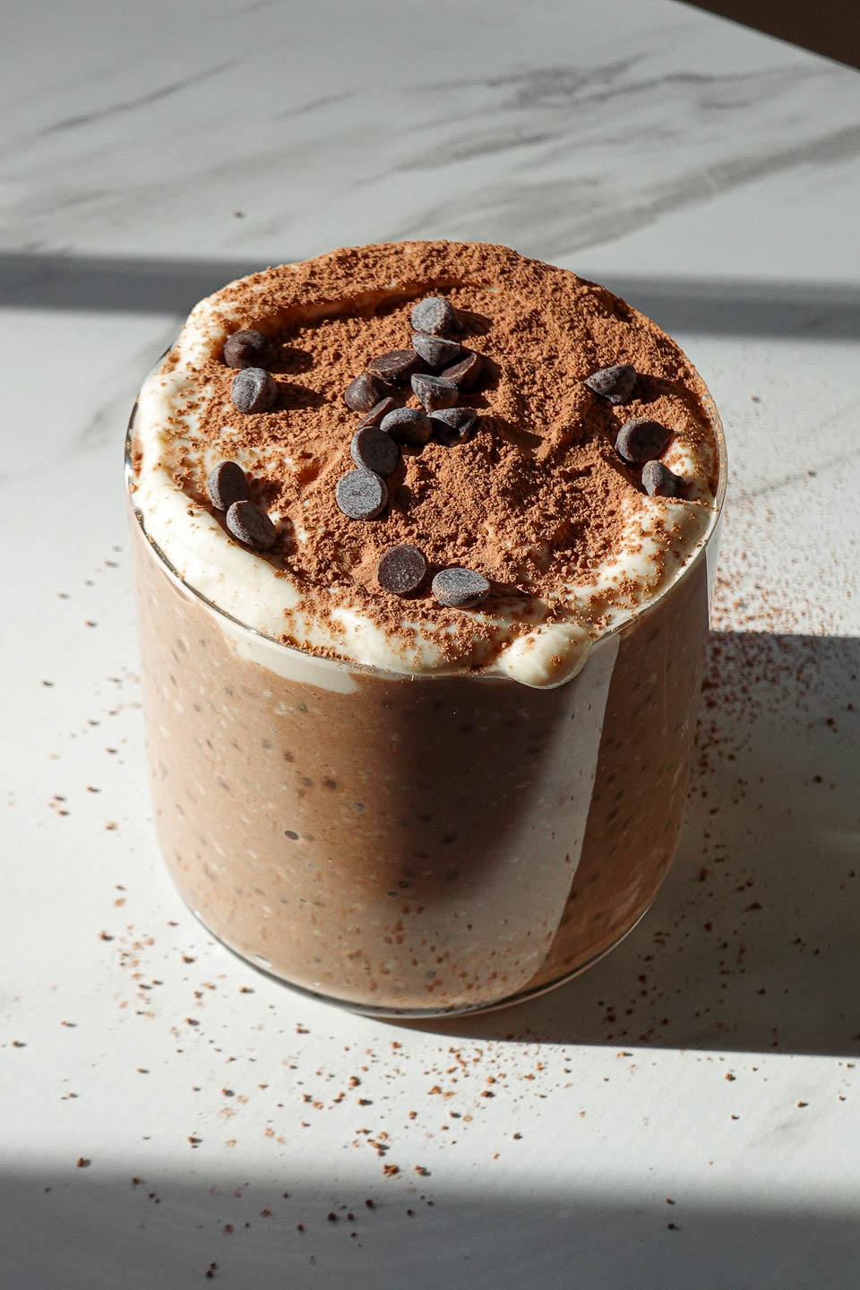 Tiramisu overnight oats in a glass jar topped with yogurt, cocoa powder, and mini chocolate chips