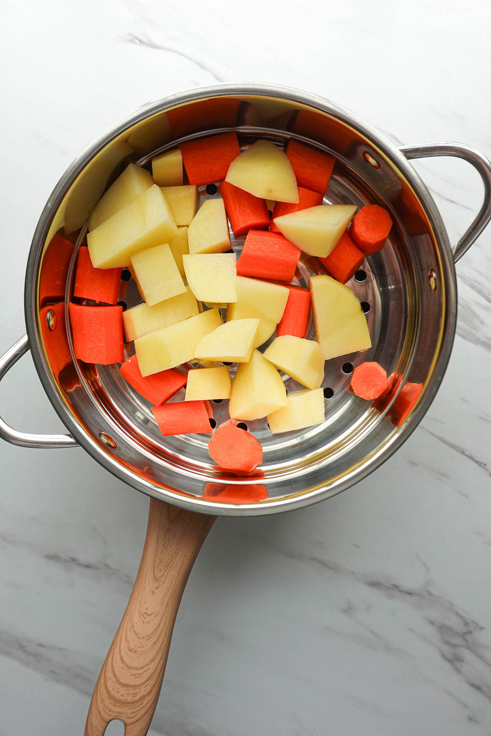 Potatoes and carrots steaming in a steamer basket