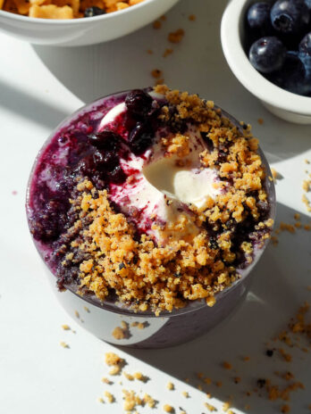 Blueberry muffin overnight oats in a glass jar topped with vegan yogurt, blueberry compote, and crushed protein cereal