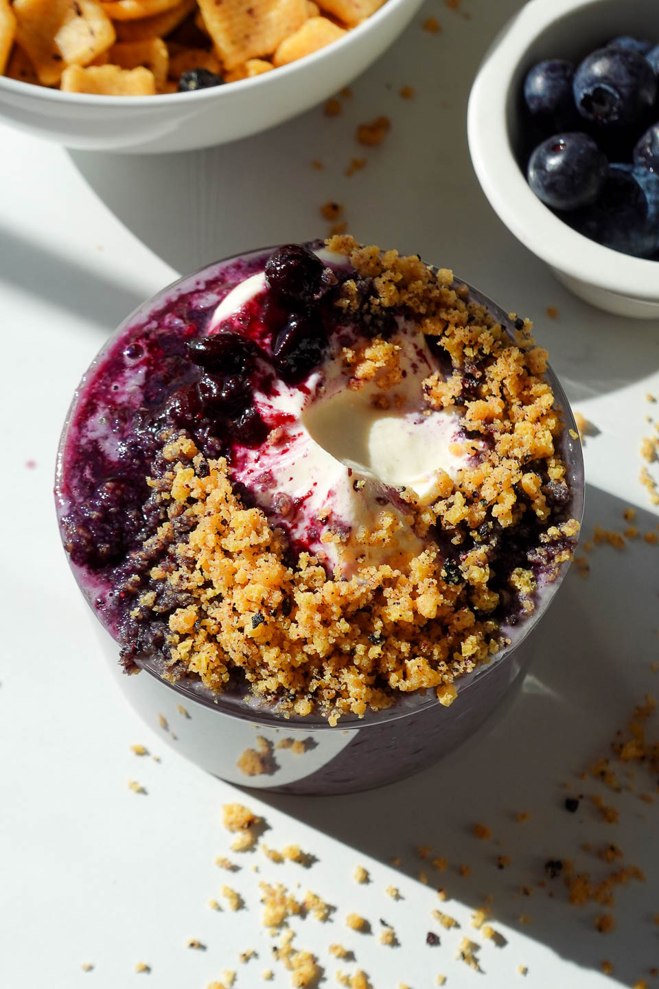 Blueberry muffin overnight oats in a glass jar topped with vegan yogurt, blueberry compote, and crushed protein cereal
