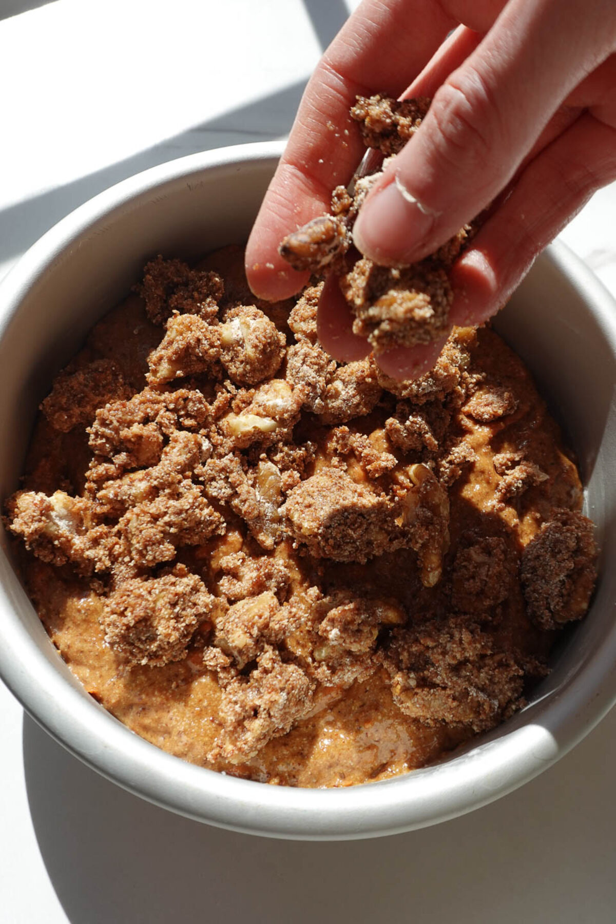 Adding walnut crumble topping over carrot coffee cake batter before baking
