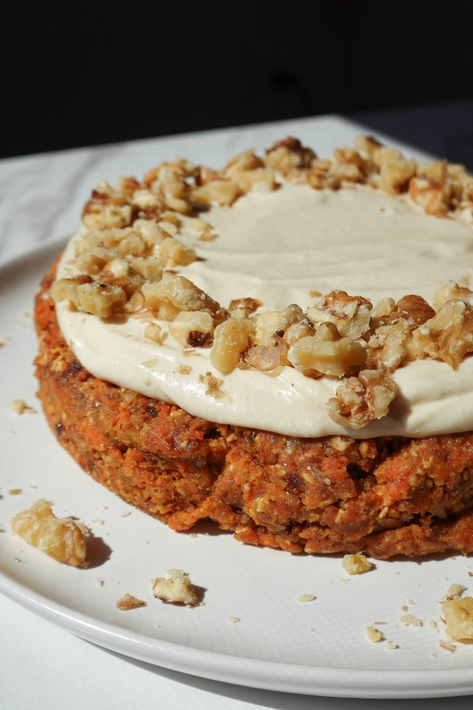 Close up of vegan carrot cake with vegan cream cheese frosting and garnished with crushed walnuts