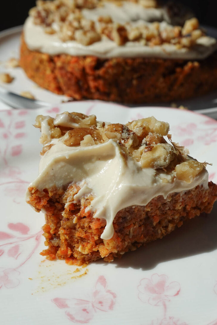 Slice of raw carrot cake showing soft, moist texture topped with vegan cream cheese frosting and chopped walnuts