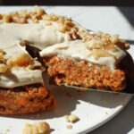 healthy no bake carrot cake topped with a vegan cream cheese frosting and crushed walnuts being sliced and served