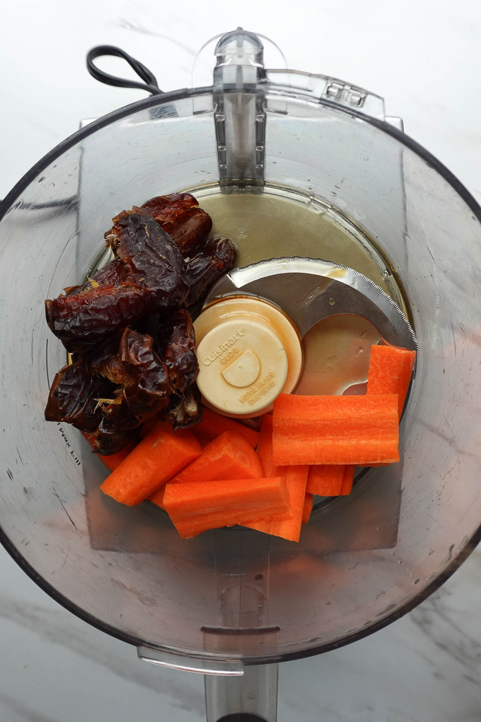 Blending dates, carrots, maple syrup, and vanilla extract in food processor for no bake carrot cake