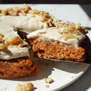 healthy no bake carrot cake topped with a vegan cream cheese frosting and crushed walnuts being sliced and served