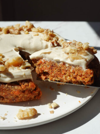 healthy no bake carrot cake topped with a vegan cream cheese frosting and crushed walnuts being sliced and served