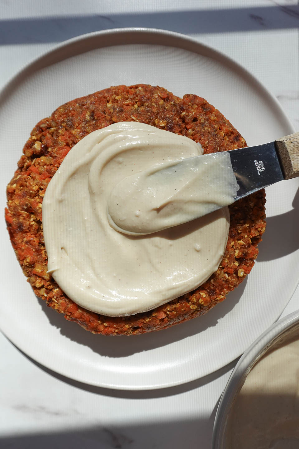 Spreading vegan cream cheese frosting over no bake carrot cake