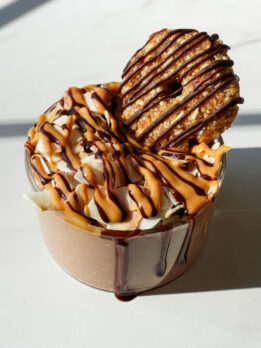Samoas overnight oats in a glass jar topped with chocolate drizzle, toasted coconut, and a homemade samoas cookie