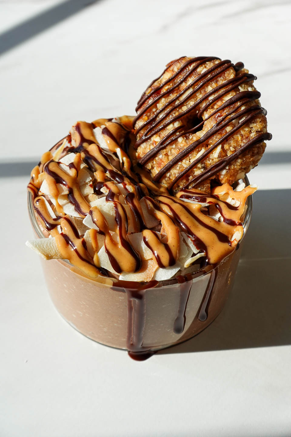 Samoas overnight oats in a glass jar topped with chocolate drizzle, toasted coconut, and a homemade samoas cookie