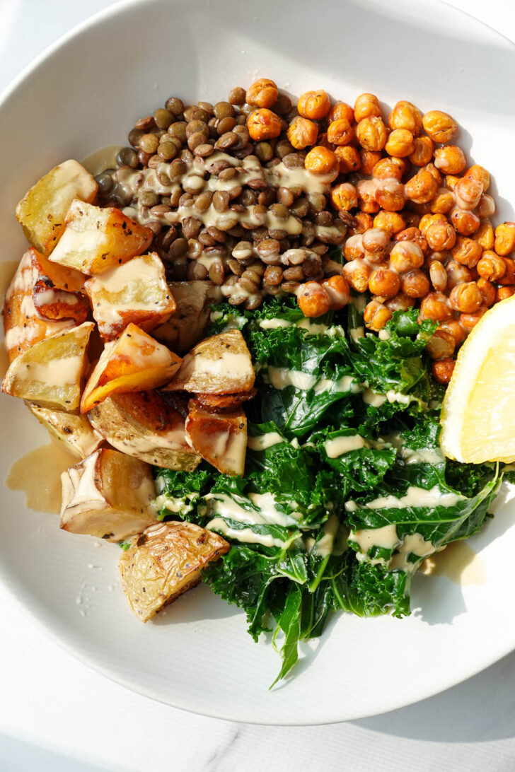 Roasted potato lentil bowl with kale and crispy chickpeas topped with lemon tahini dressing
