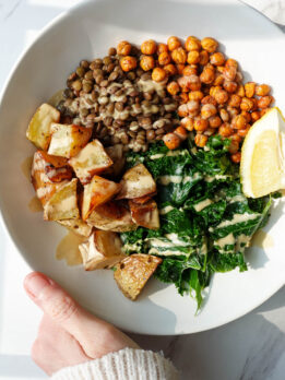 Warm kale salad with lentils, roasted potatoes, crispy chickpeas, and lemon tahini dressing in a bowl