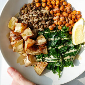 Warm kale salad with lentils, roasted potatoes, crispy chickpeas, and lemon tahini dressing in a bowl