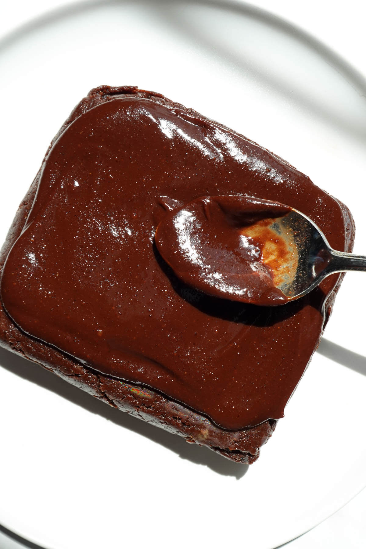 Using a spoon to spread the chocolate ganache on top of the vegan cosmic brownie.