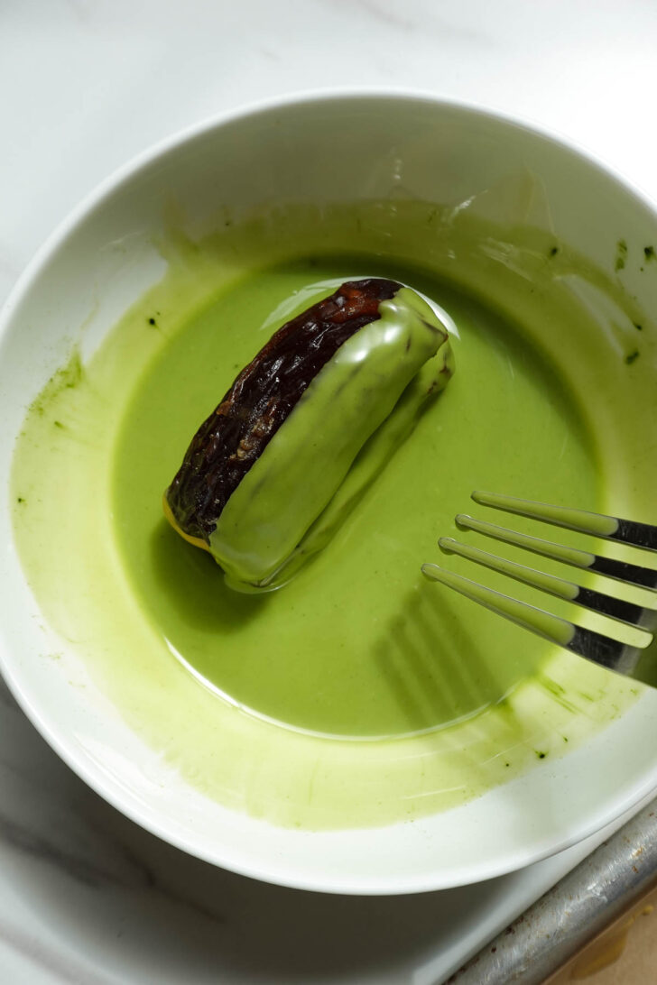 Dipping stuffed dates into melted matcha white chocolate coating.