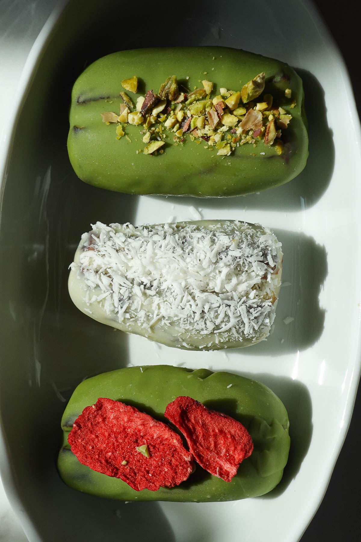 Pistachio matcha stuffed dates with assorted toppings including crushed pistachios, shredded coconut, and freeze dried strawberries.