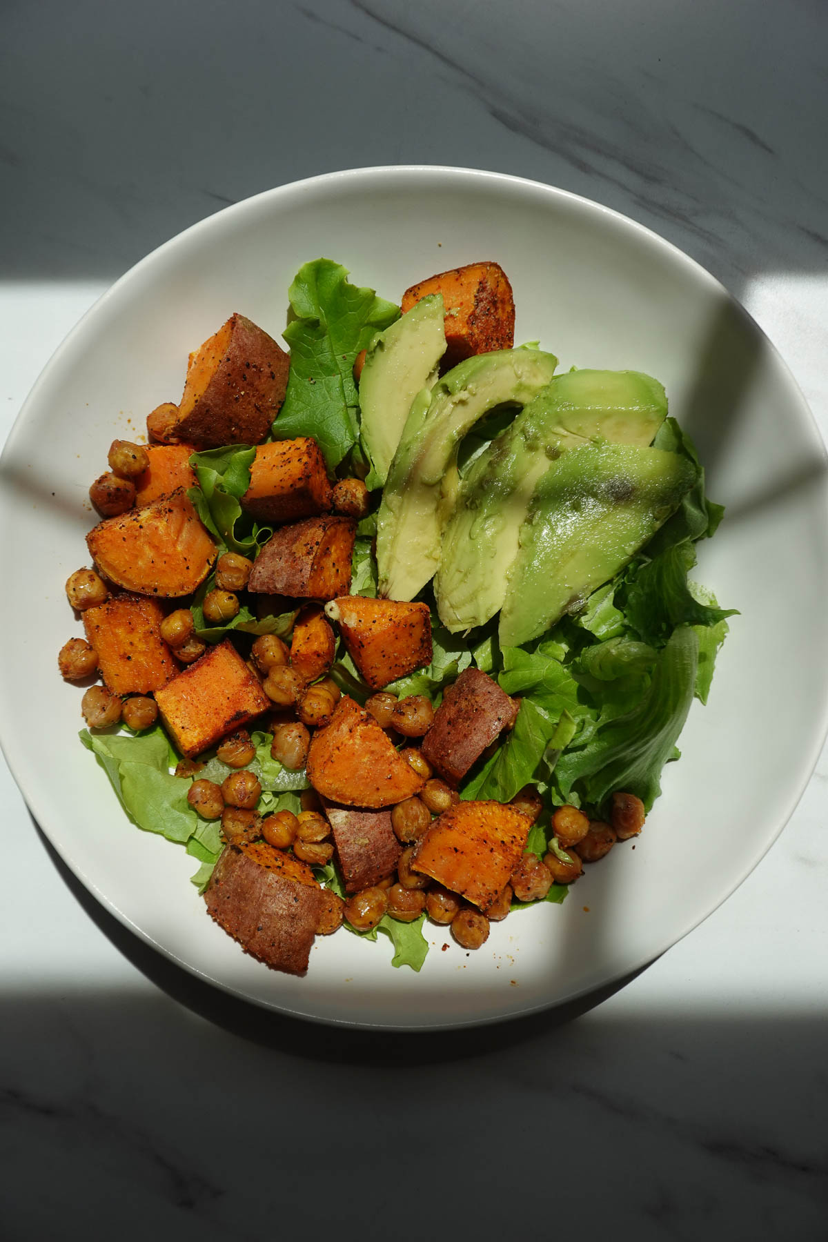 Salad topped with roasted sweet potatoes, crispy chickpeas, and sliced avocado.