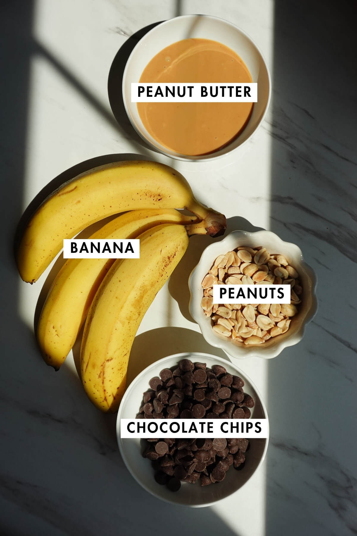 Ingredients for frozen snickers banana pops including bananas, peanut butter, peanuts, and chocolate chips.