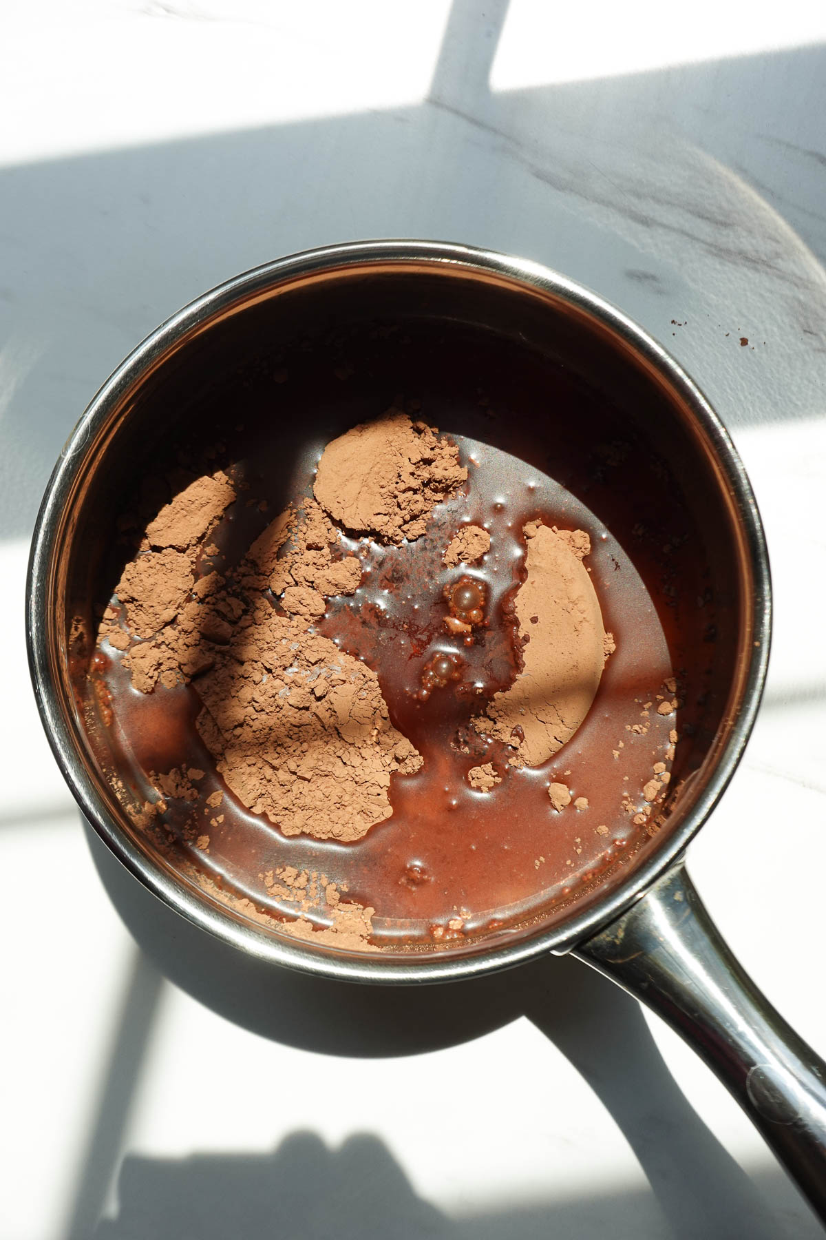 Cocoa powder, maple syrup, water, vanilla extract, and sea salt added to a saucepan to make homemade chocolate syrup.