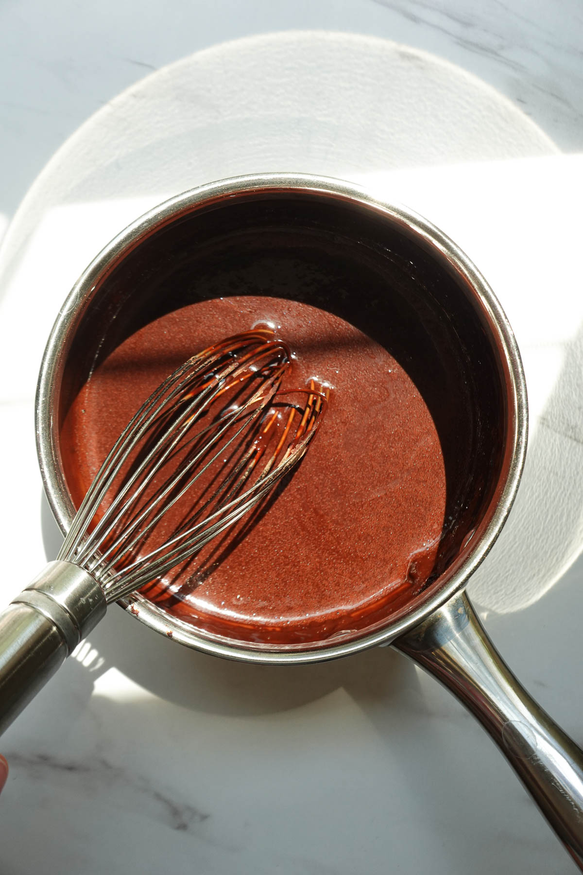 Whisking cocoa powder and other ingredients together in a saucepan to make chocolate syrup.