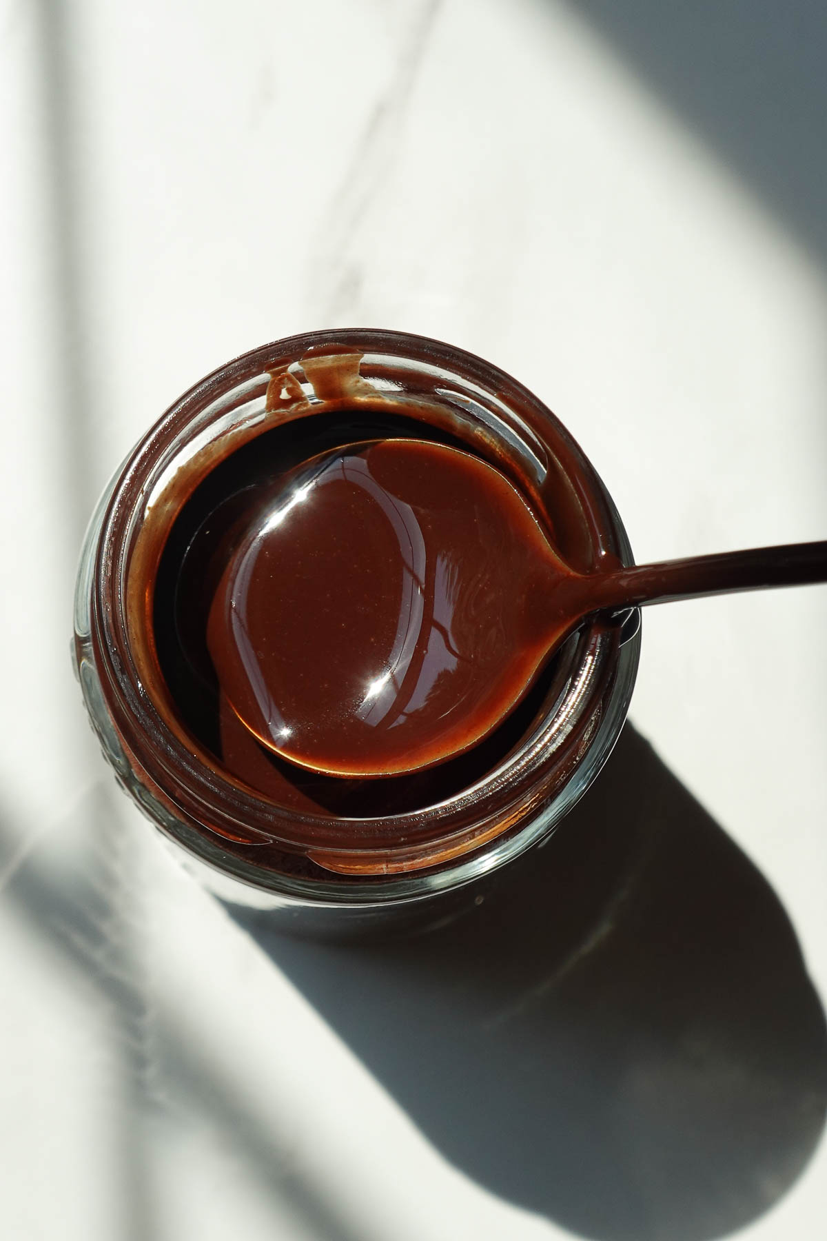 Healthy homemade chocolate syrup in a glass jar with a spoon.