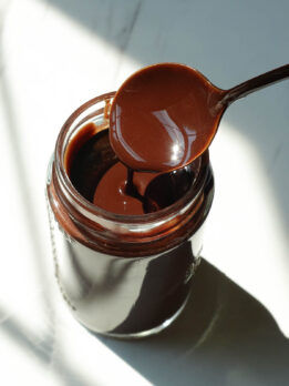 Homemade chocolate syrup drizzled from a spoon, showing its thick and smooth chocolate texture.