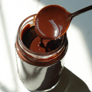 Homemade chocolate syrup drizzled from a spoon, showing its thick and smooth chocolate texture.