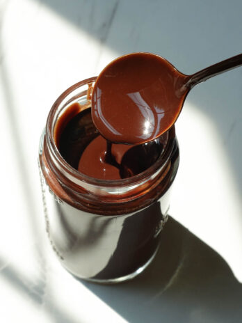 Homemade chocolate syrup drizzled from a spoon, showing its thick and smooth chocolate texture.