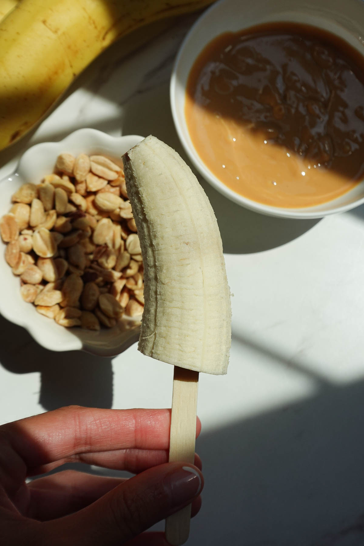 Banana half on popsicle sticks ready to make snickers banana pops.
