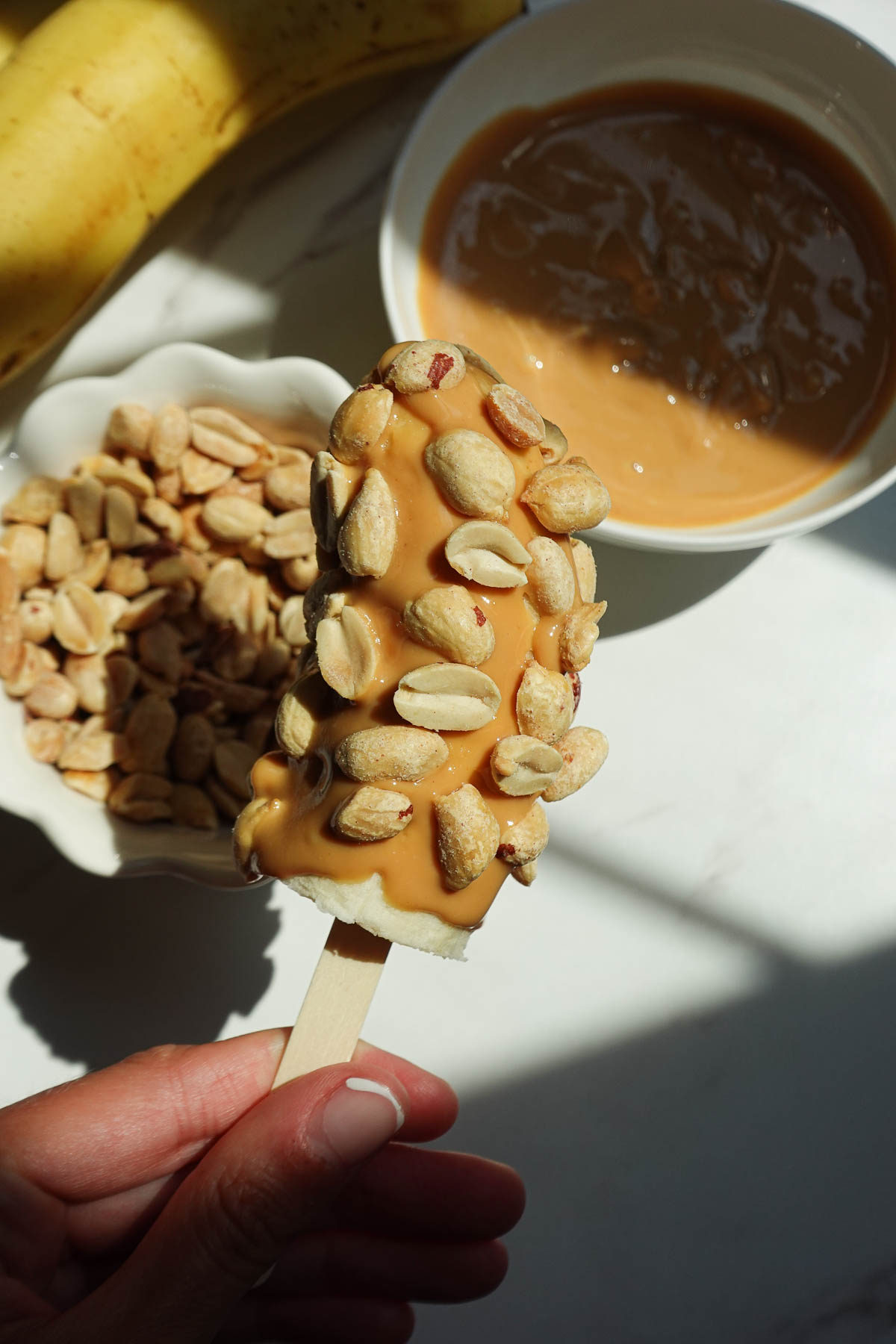 Pressing chopped peanuts into peanut butter-coated bananas.