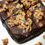 Sliced walnut date brownies on a plate, topped with vegan chocolate and walnuts.