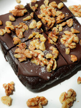 Sliced walnut date brownies on a plate, topped with vegan chocolate and walnuts.