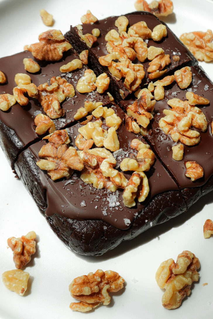 Sliced walnut date brownies on a plate, topped with vegan chocolate and walnuts.