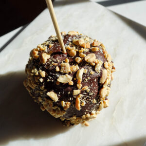 Chocolate-covered date caramel apple topped with chopped peanuts.