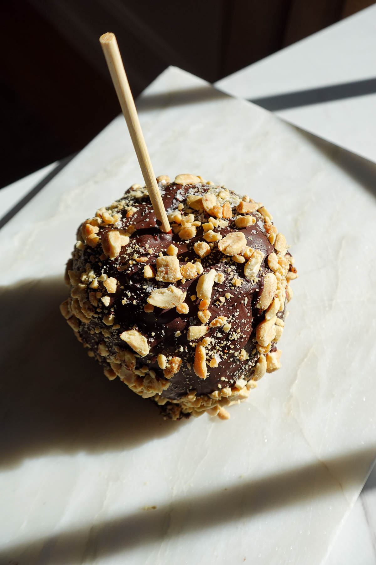 Chocolate-covered date caramel apple topped with chopped peanuts.