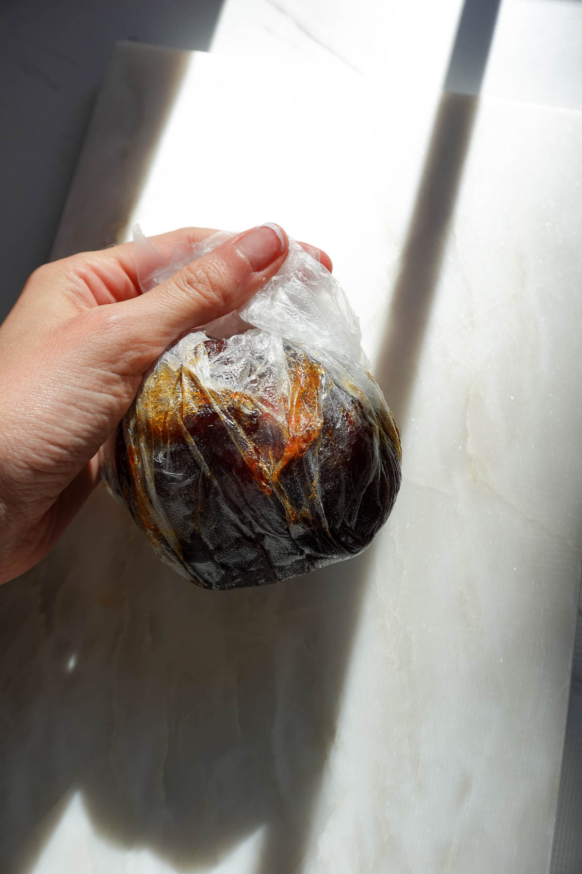 Using plastic wrap to press flattened medjool dates around an apple.