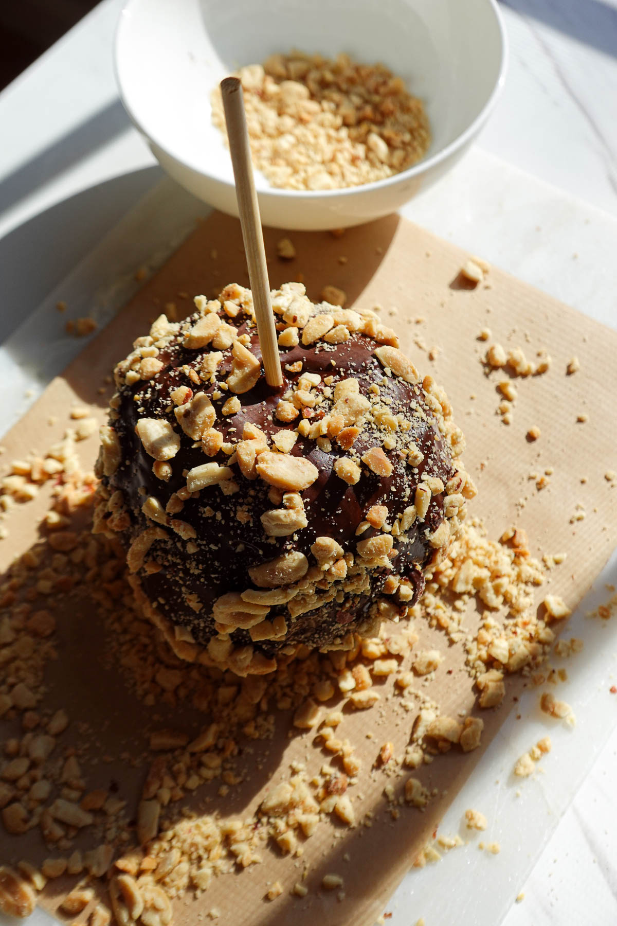 Sprinkling chopped peanuts over the chocolate covered apple.