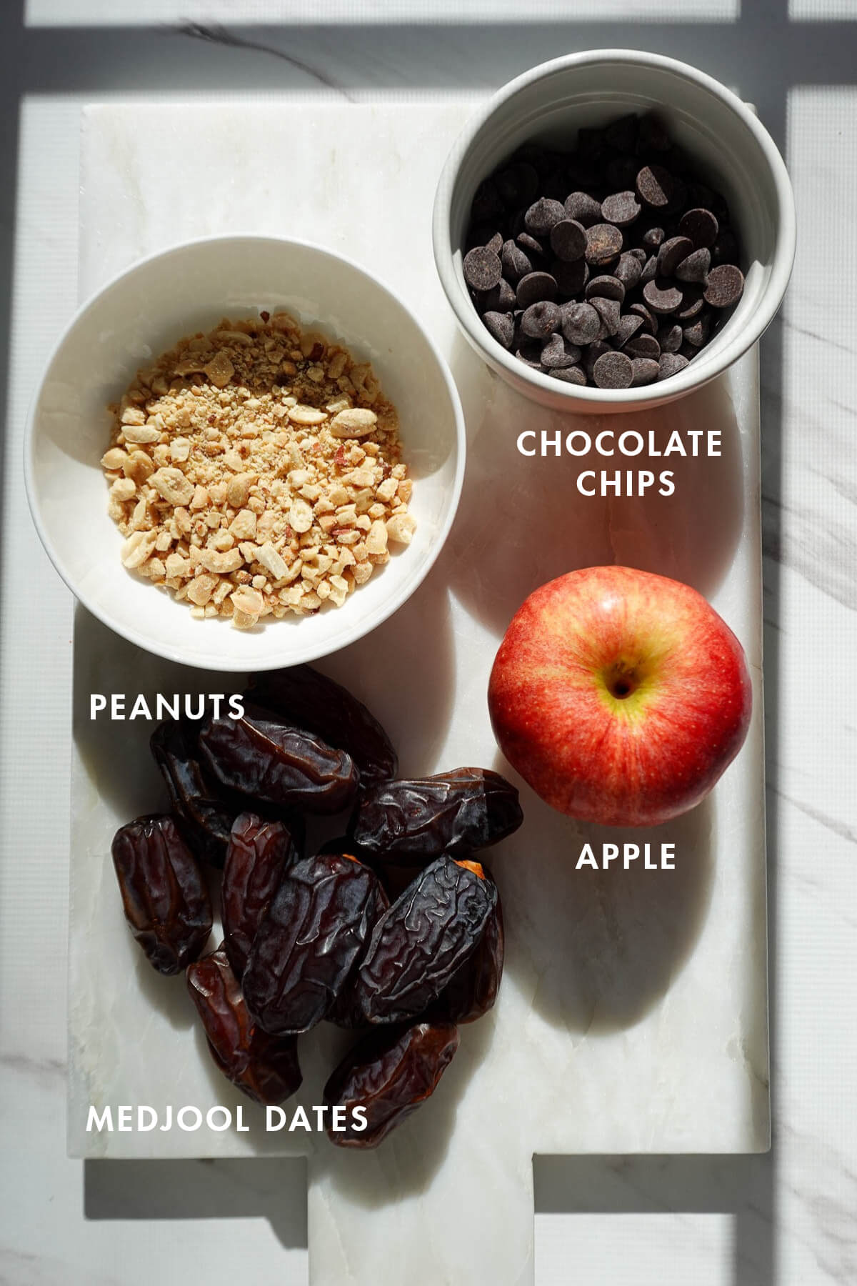 Measured ingredients needed to make date caramel apple including apple, medjool dates, chocolate chips, and peanuts.