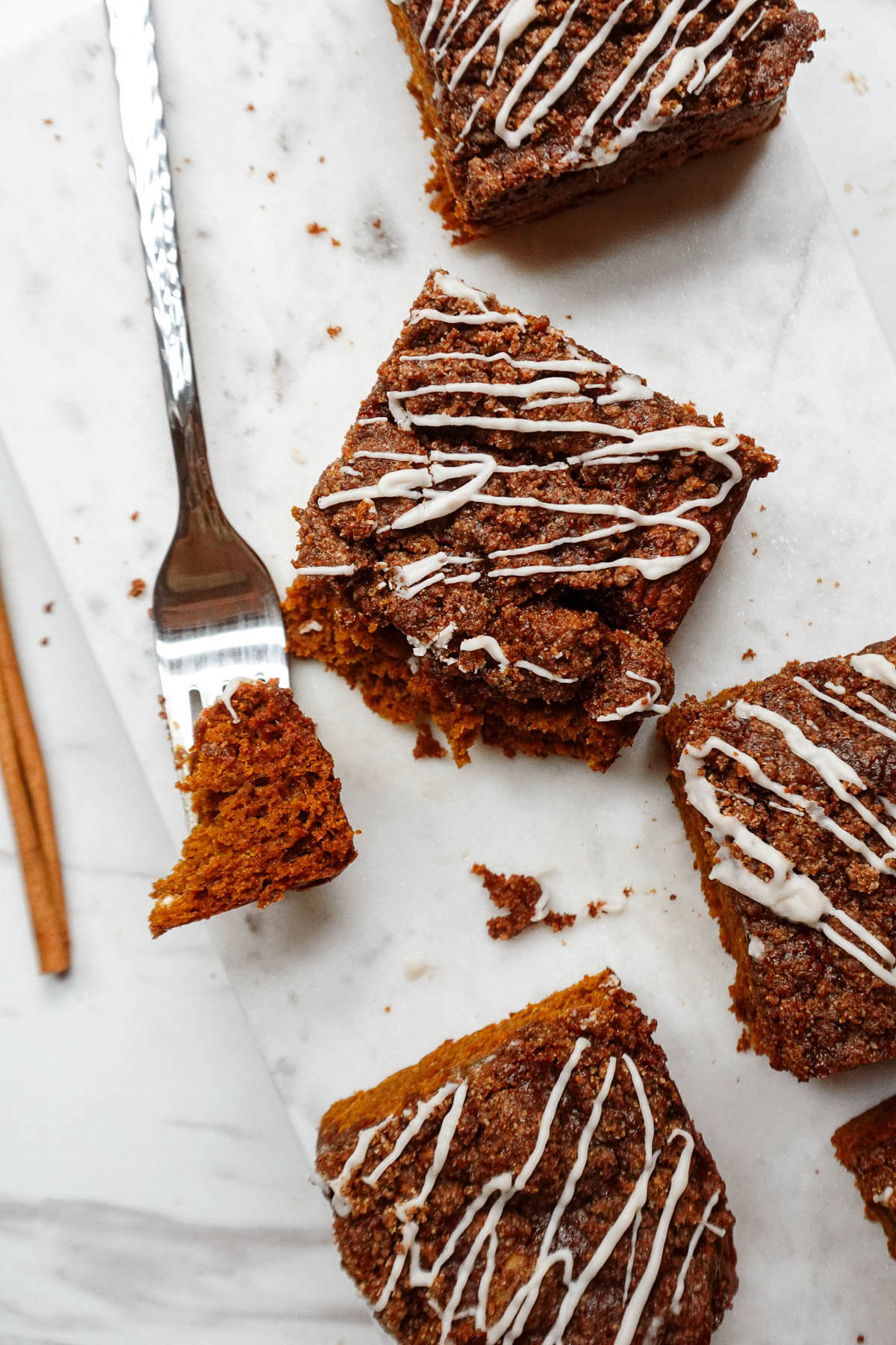 Slices of vegan pumpkin coffee cake on a marble tray with a fork bite taken out.