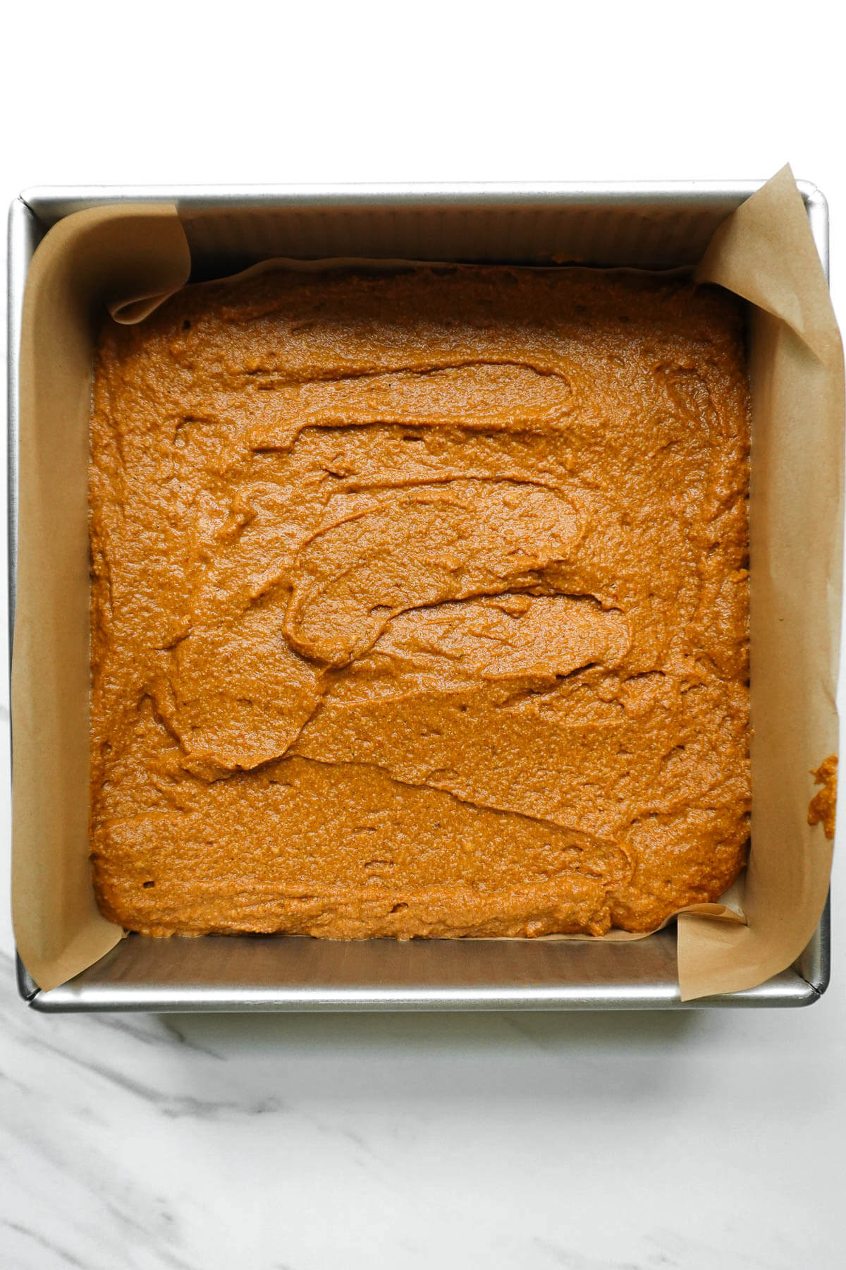 Pumpkin coffee cake batter spread into a parchment-lined square pan.