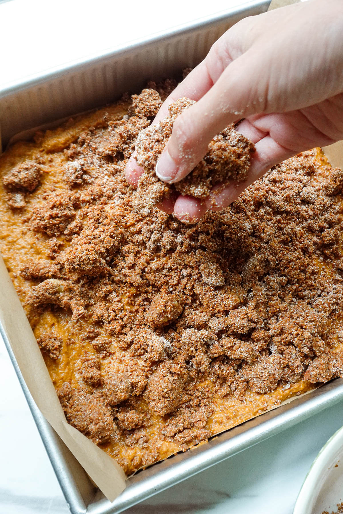Sprinkling cinnamon-walnut streusel on top of pumpkin coffee cake batter.