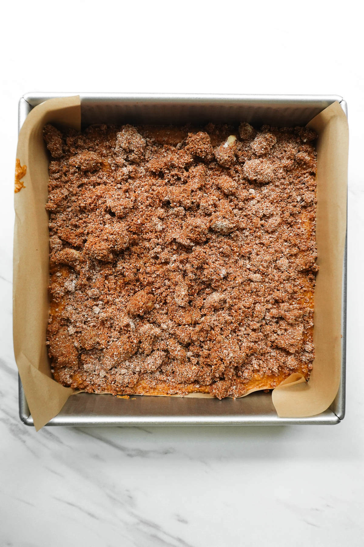 Pumpkin coffee cake batter spread into a parchment-lined square pan and topped with cinnamon-walnut streusel.