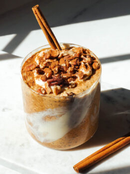 Pumpkin overnight oats in a glass jar topped with vegan yogurt, chopped pecans and a cinnamon stick.
