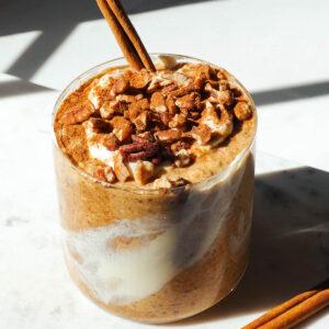 Pumpkin overnight oats in a glass jar topped with vegan yogurt, chopped pecans and a cinnamon stick.