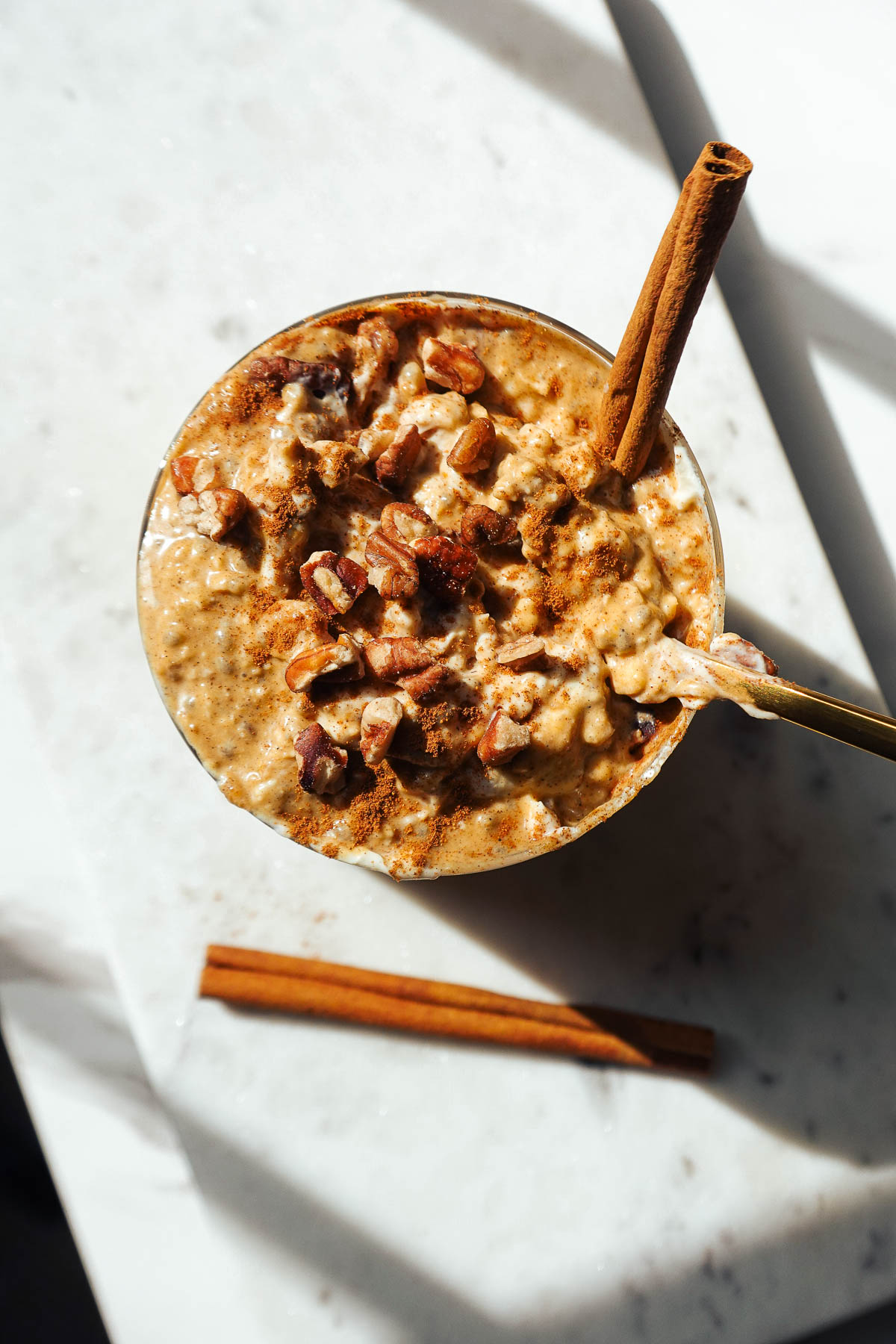 Pumpkin overnight oats in a glass jar topped with vegan yogurt, chopped pecans and a cinnamon stick.